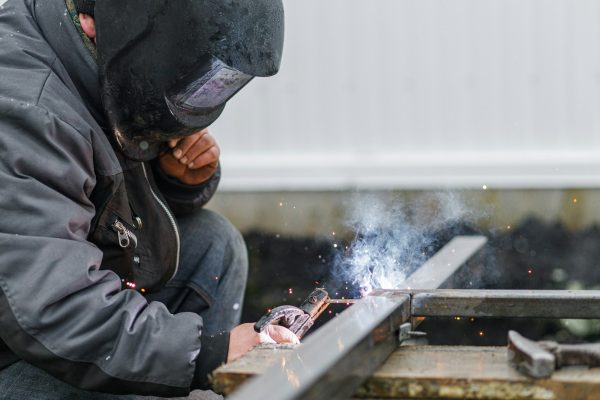 Shielded metal arc welding. Worker welding metal with electrodes, wearing protective helmet